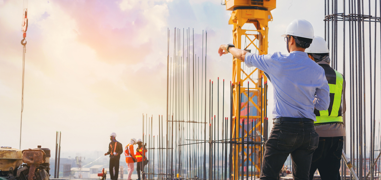 Structural engineer and foreman worker discuss plans outdoors at building construction site.