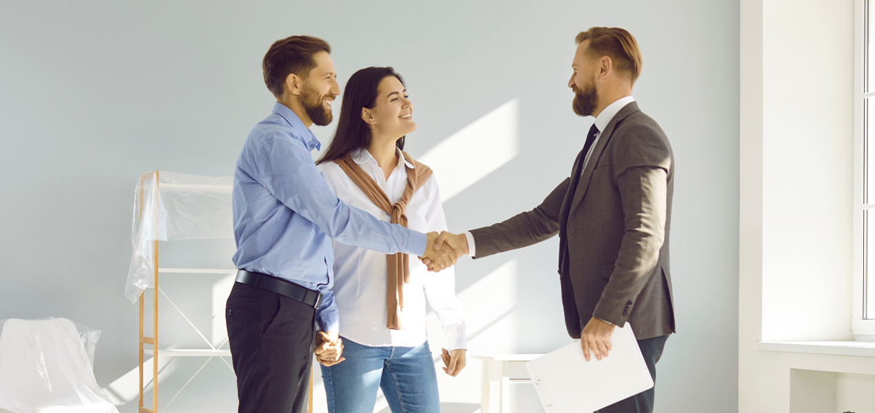 A couple and a man in business attire shaking hands in an office, representing a formal agreement