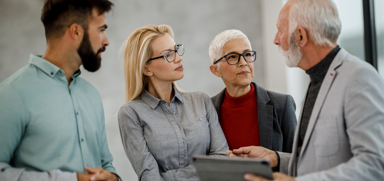 A group of business people are standing, having a discussion after looking at a tablet.