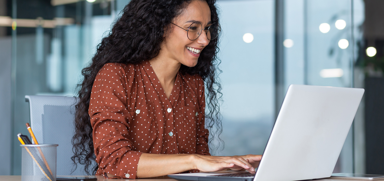A Hispanic woman working on a laptop in a modern office setting.