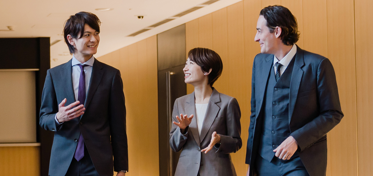 Three business professionals engaged in conversation in a modern office hallway.