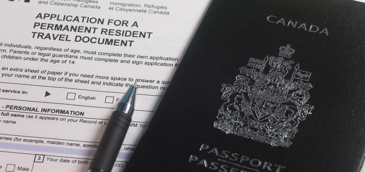 A Canadian passport lies on top of an application form for a permanent resident travel document. A black pen is placed on the form, which is issued by Immigration, Refugees, and Citizenship Canada.