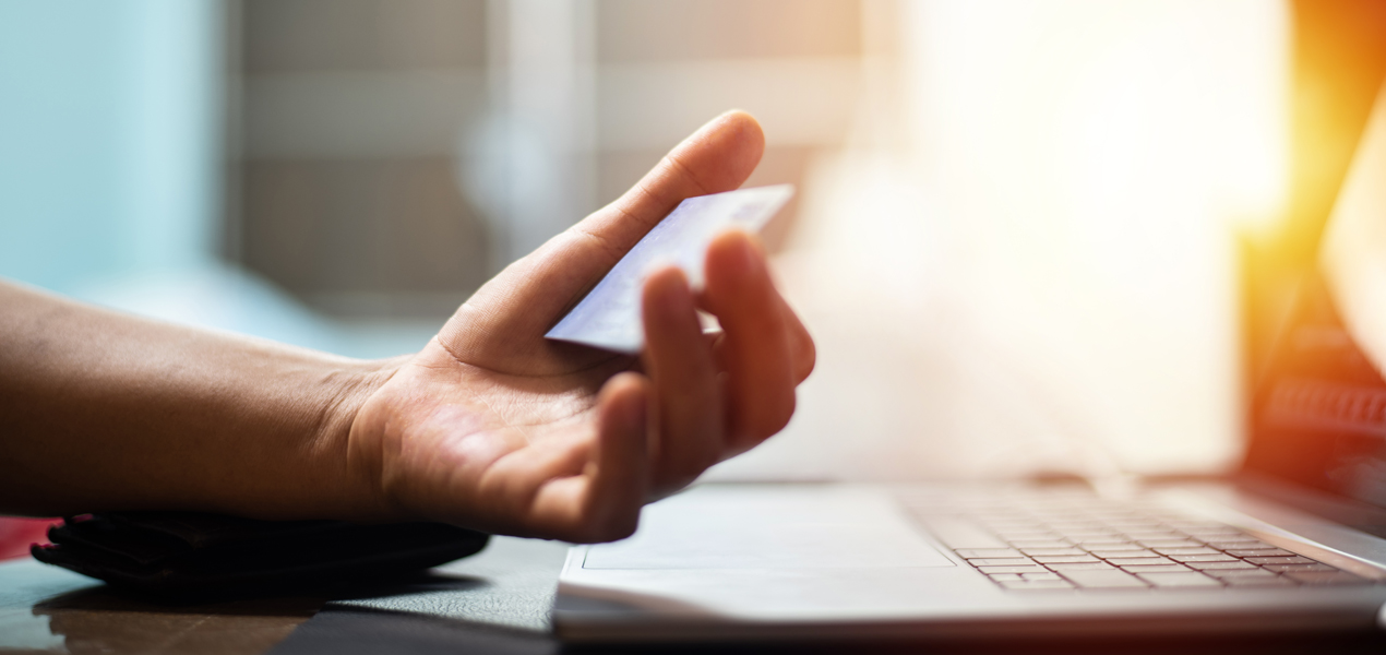 A hand holds a credit card in front of an open laptop, suggesting online shopping or payment processing.
